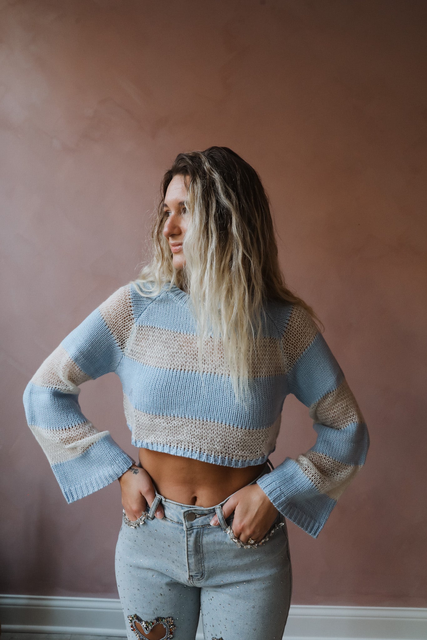 This knit sweater top features a light blue and cream color combination, with cropped length and long sleeves for a versatile and stylish look.